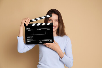 Making movie. Smiling woman with clapperboard on beige background