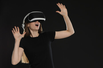 Surprised woman using virtual reality headset on black background, space for text