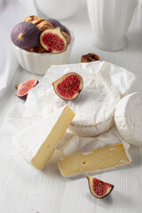 Camembert cheese with figs on a white table.