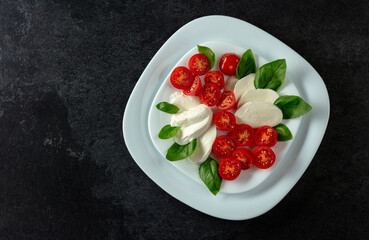 Mozzarella with basil and cherry tomatoes on a black background.