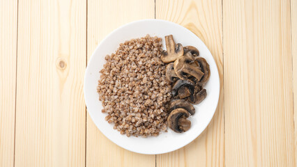 Buckwheat porridge with fried mushrooms on a plate on a wooden background. Healthy diet food. The concept of healthy eating