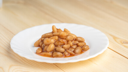 baked beans in sauce on a white plate close-up on a wooden background. the view from the top.