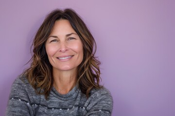 Fototapeta premium Portrait of a content woman in her 40s smiling at the camera in front of pastel purple background