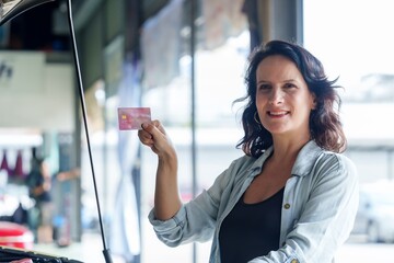 Woman holding credit card, smiling at auto repair shop. Highlights financial transaction, satisfaction, and customer service. Emphasizes positive experience and professional automotive service.