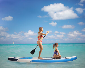 Full length profile shot of a young woman in bikini paddling on a SUP board with a child