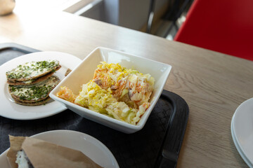 A close-up shot of a simple lunch of creamy salad and herb-topped flatbreads. The salad is served in a white bowl, while the flatbreads are piled on a white plate. The table is a light wood color.
