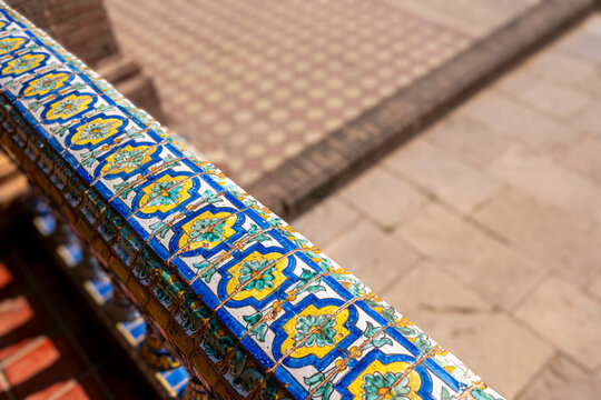 Detailed ceramic tiles in vibrant blues and yellows adorn a balustrade, showcasing the artistic heritage of Seville, Andalusia, Spain
