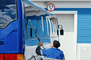 A man is cleaning a bus with a squeegee. The bus is parked in front of a building with a sign that...