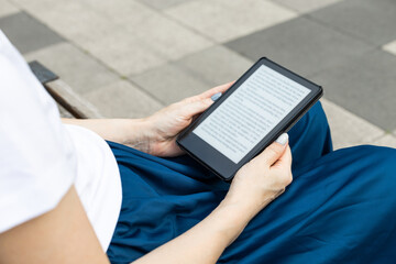 woman reading an e-book sitting on a park bench.  reading a book outdoors. 