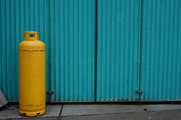 Obraz premium Used large yellow gas cartridge stands in front of a turquoise corrugated iron wall in an industrial area
