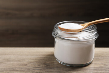 Baking soda in glass jar on wooden table, space for text