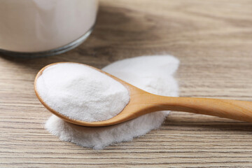 Baking soda in spoon on wooden table, closeup
