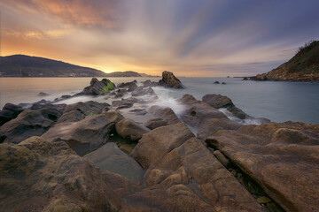 Warm sunset in Kantarepe cove, in Algorta, with a sky of intense colors and sea water between the rocks in the foreground