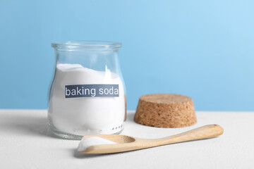 Baking soda in glass jar and spoon on white table