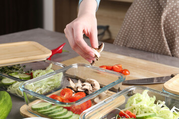 Healthy food. Woman putting pieces of champignons into glass container at grey table in kitchen, closeup
