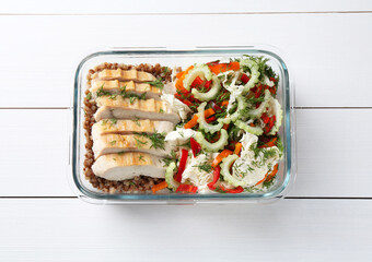 Healthy meal. Chicken breast, buckwheat and salad in container on white wooden table, top view