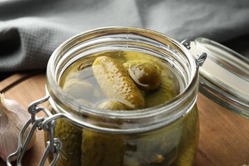 Pickled cucumbers in jar on wooden board, closeup
