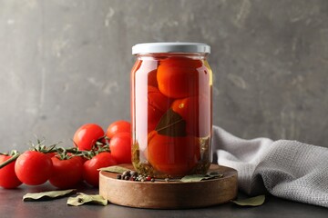 Tasty pickled tomatoes in jar, spices and fresh vegetables on grey table