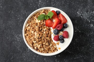 Tasty granola with berries and yogurt in bowl on dark textured table, top view