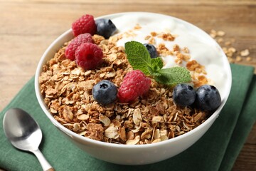 Tasty granola with berries and yogurt in bowl on wooden table, closeup