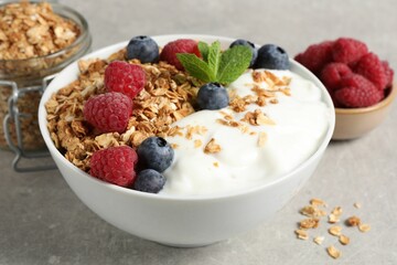Tasty granola with berries and yogurt in bowl on grey textured table, closeup