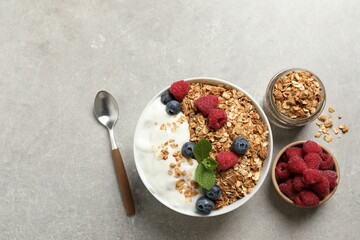 Tasty granola with berries and yogurt served on grey textured table, flat lay. Space for text