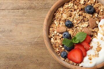 Tasty granola with berries, almond and yogurt in bowl on wooden table, top view. Space for text