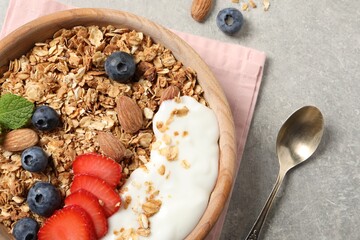 Tasty granola with berries, almond and yogurt served on grey textured table, flat lay