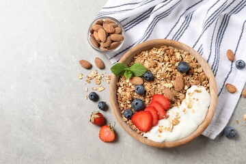 Tasty granola with berries, almond and yogurt in bowl on grey textured table, flat lay. Space for text