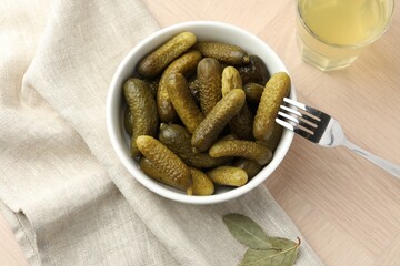 Pickled cucumbers in bowl, fork and brine on wooden table, flat lay