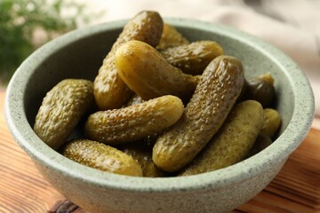 Pickled cucumbers in bowl on wooden board, closeup