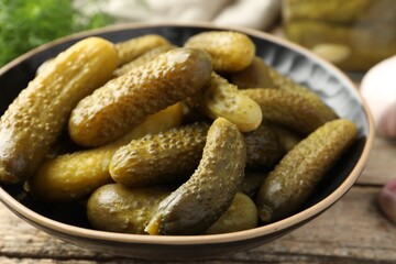 Pickled cucumbers in bowl on wooden table, closeup