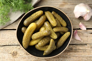 Pickled cucumbers in bowl, garlic and dill on wooden table, flat lay