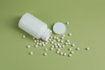 Homeopathic remedy and bottle on light green background, top view