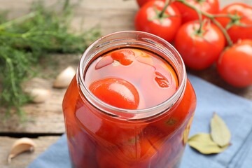 Tasty pickled tomatoes in jar, spices and fresh vegetables on wooden table, closeup