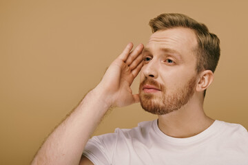 A stylishly dressed man with a beard places his hand on his face, contemplating deeply.