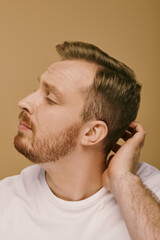 A stylish man with a goatee touching his hair carefully.