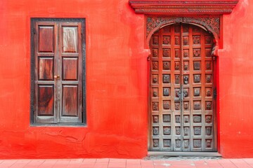Obraz premium Vivid red wall with traditional wooden door and ornate iron gate
