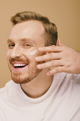 Obraz premium A man in casual attire is happily applying cream to his face.