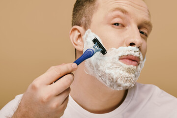 A man in casual attire carefully shaves his face with a razor.