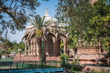 Naklejka premium Ancient Indian Temples of structure featuring intricate carvings and vibrant floral foreground, Mandore Gardens, Jodhpur, Rajasthan, India