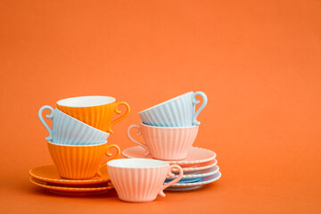 Stacked light blue and pink coffee cups with saucers against orange background with copy space.
