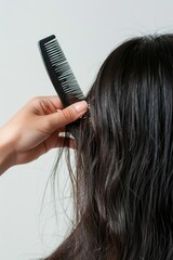 Fototapeta premium Close-up of a woman's hands combing her hair with a black comb, possibly in a beauty or grooming setting