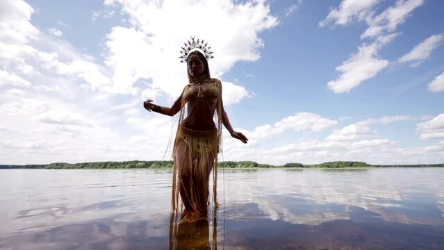 Clear and calm water reflects the sky and clouds. A woman in an exotic costume and a crown on her head dances in the water, creating an atmosphere of freedom.