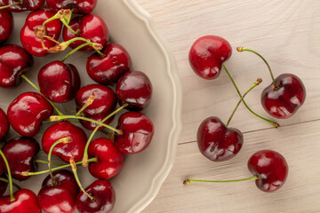 Several ripe sweet cherries with ceramic plate on wooden table, macro, top view.