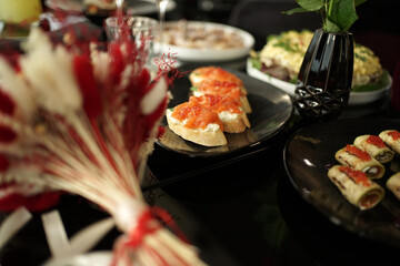 Sandwiches with red fish and other cold snacks on a black table.