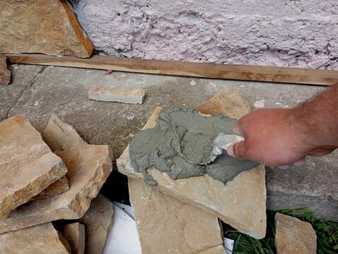 A person applies a special glue to the surface of a natural stone with a special spatula. The process of decorating walls with glue.
