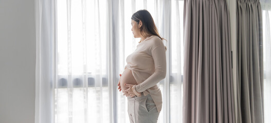 Pregnant asian woman holds hands on belly touching her baby caring about her health Beautiful happy pregnant woman tender mood photo of pregnancy