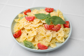 Tasty pasta with tomato, cheese and basil on white tiled table