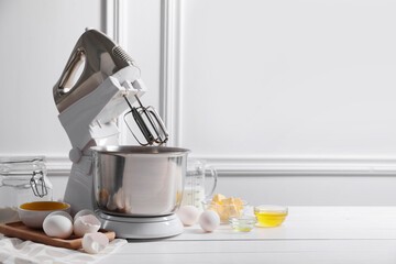 Modern stand mixer and ingredients for dough on white table indoors. Space for text